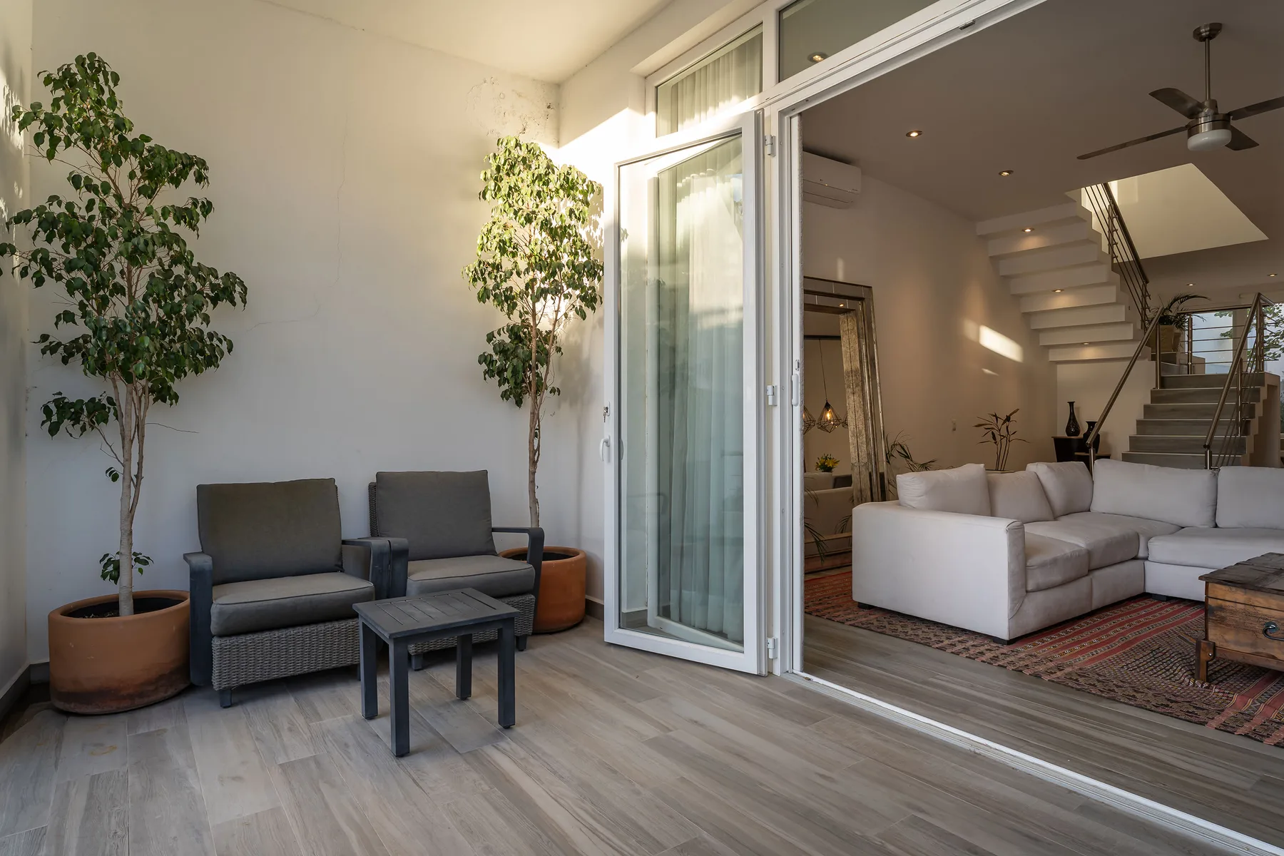 A bright patio seating area opens into a living room with a staircase.