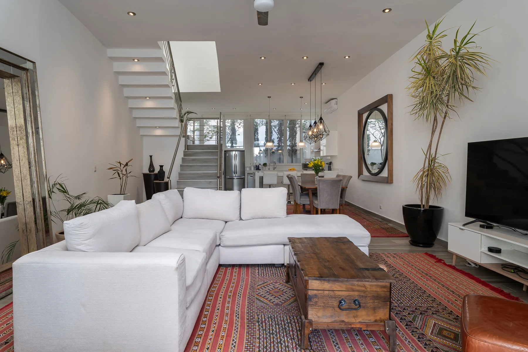 A bright living room with white seating, a wooden coffee table, and a patterned rug.