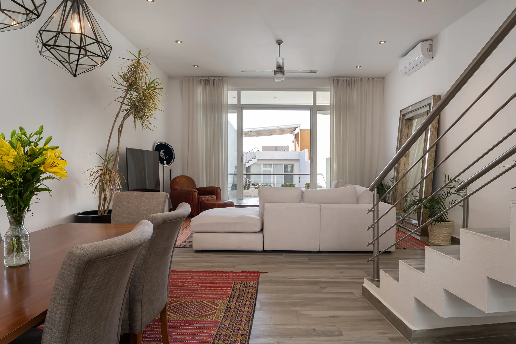 A bright living room with a seating area beside a staircase and large windows.