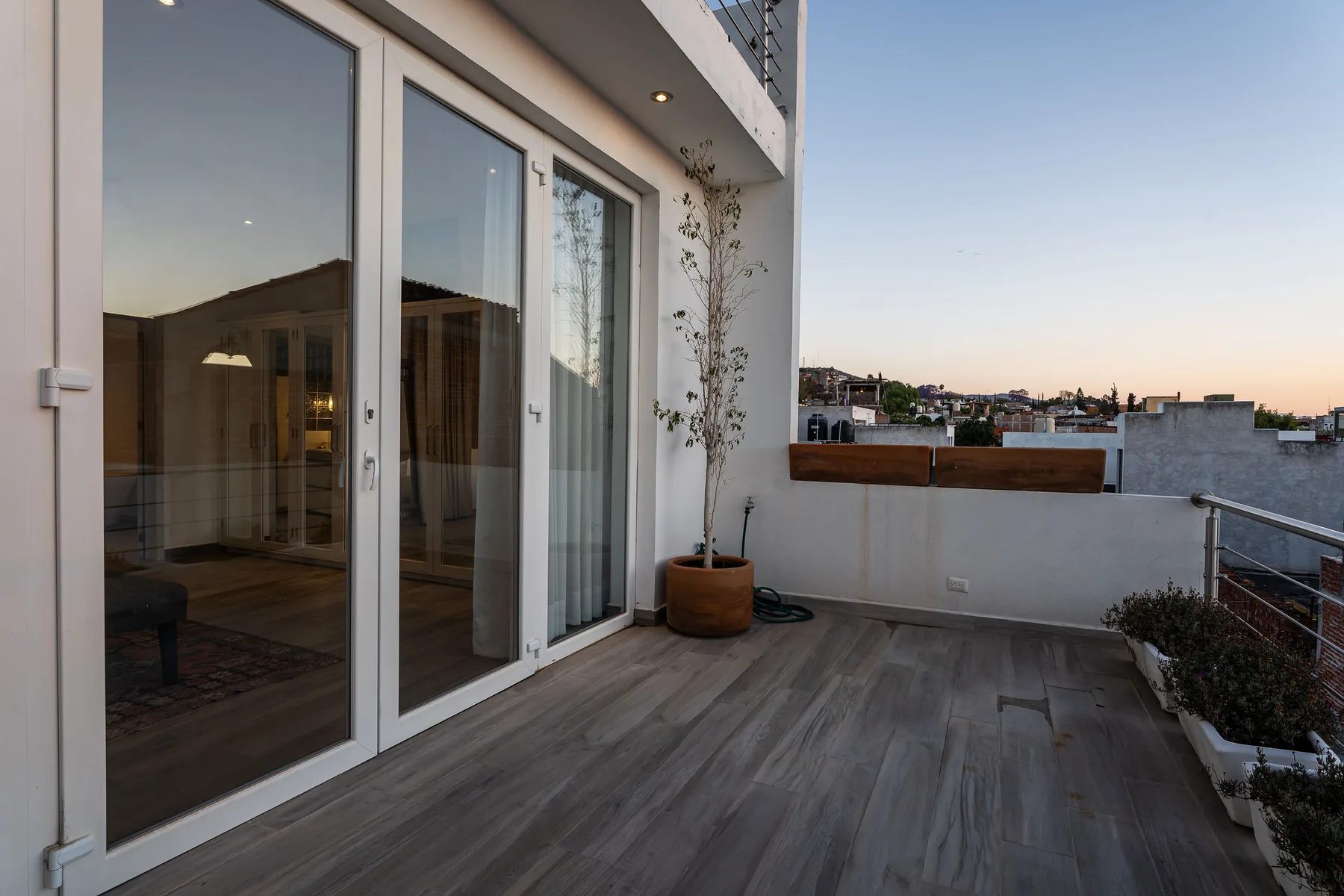 A rooftop terrace with a wide sliding glass door and a view of nearby buildings.