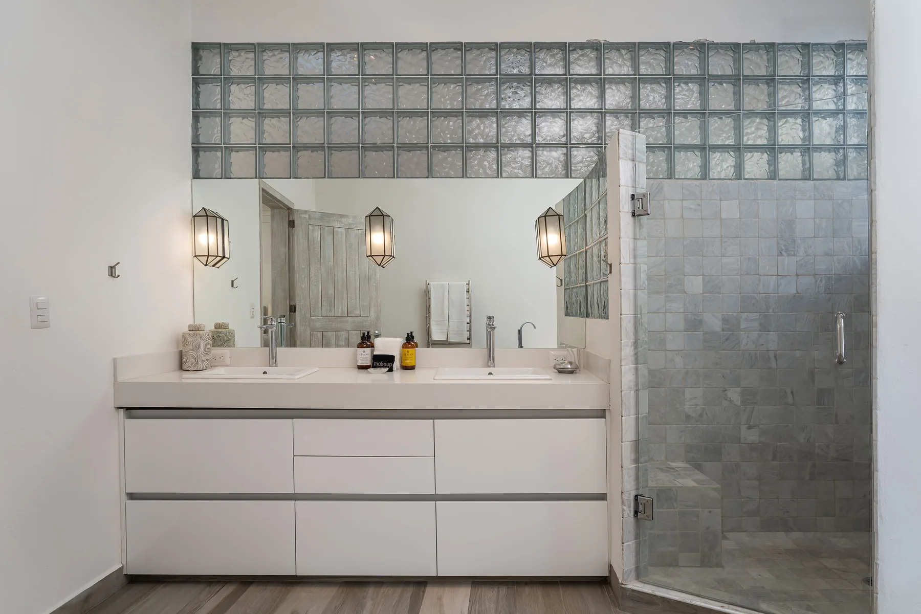 A bathroom vanity with a wide mirror stands beside a tiled shower.