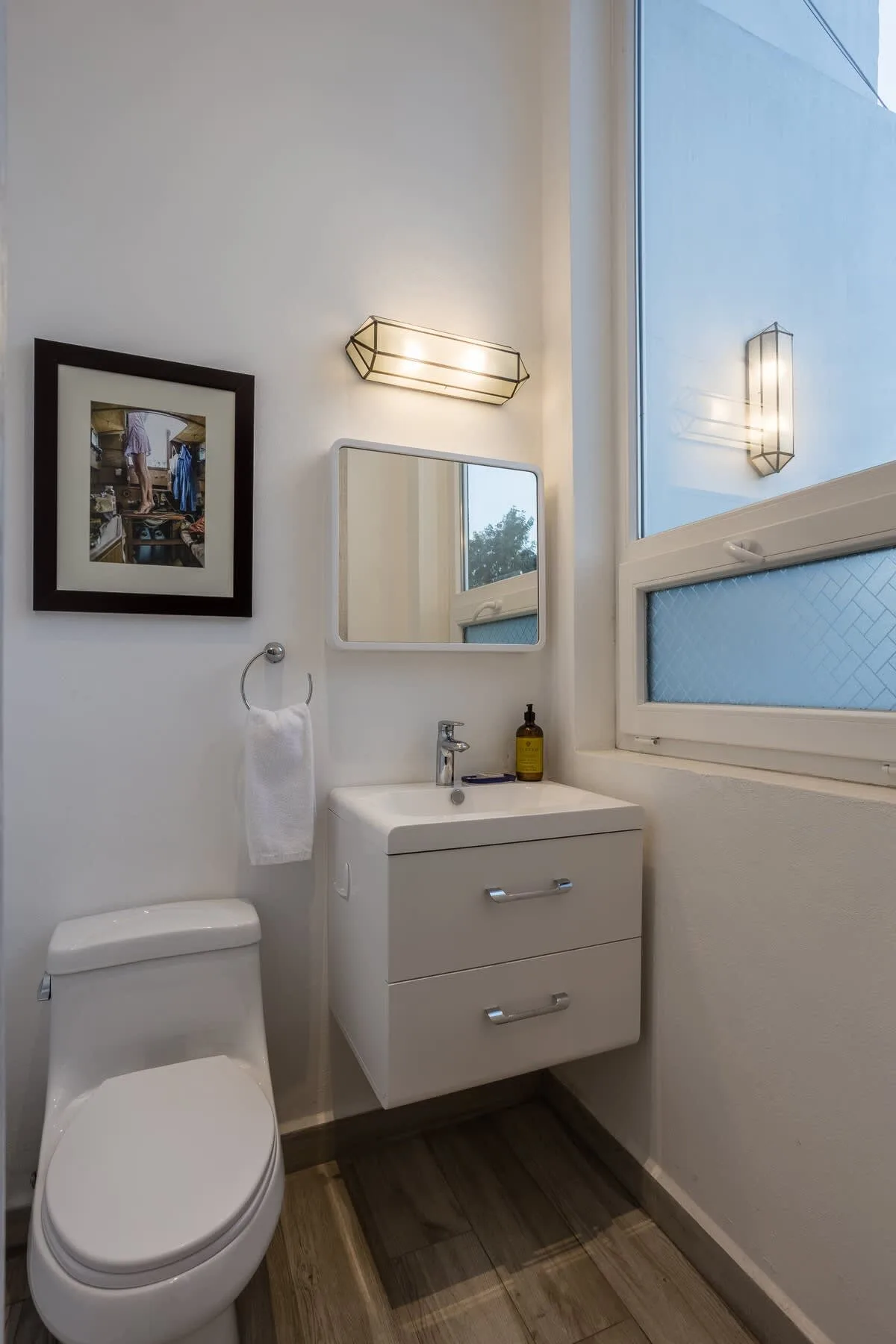 A bright bathroom with a toilet, floating vanity, and large window.