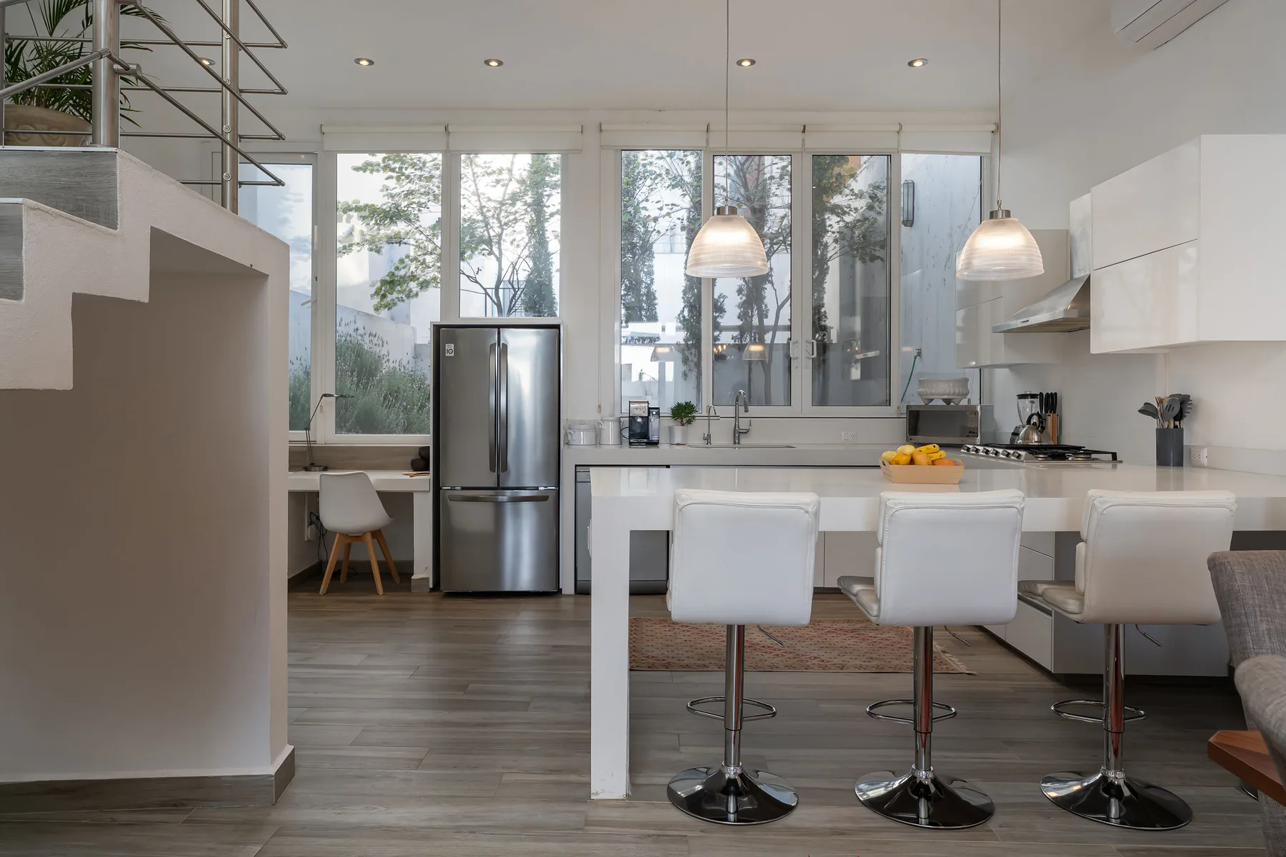 A bright kitchen and dining area with a counter, seating, and large windows.