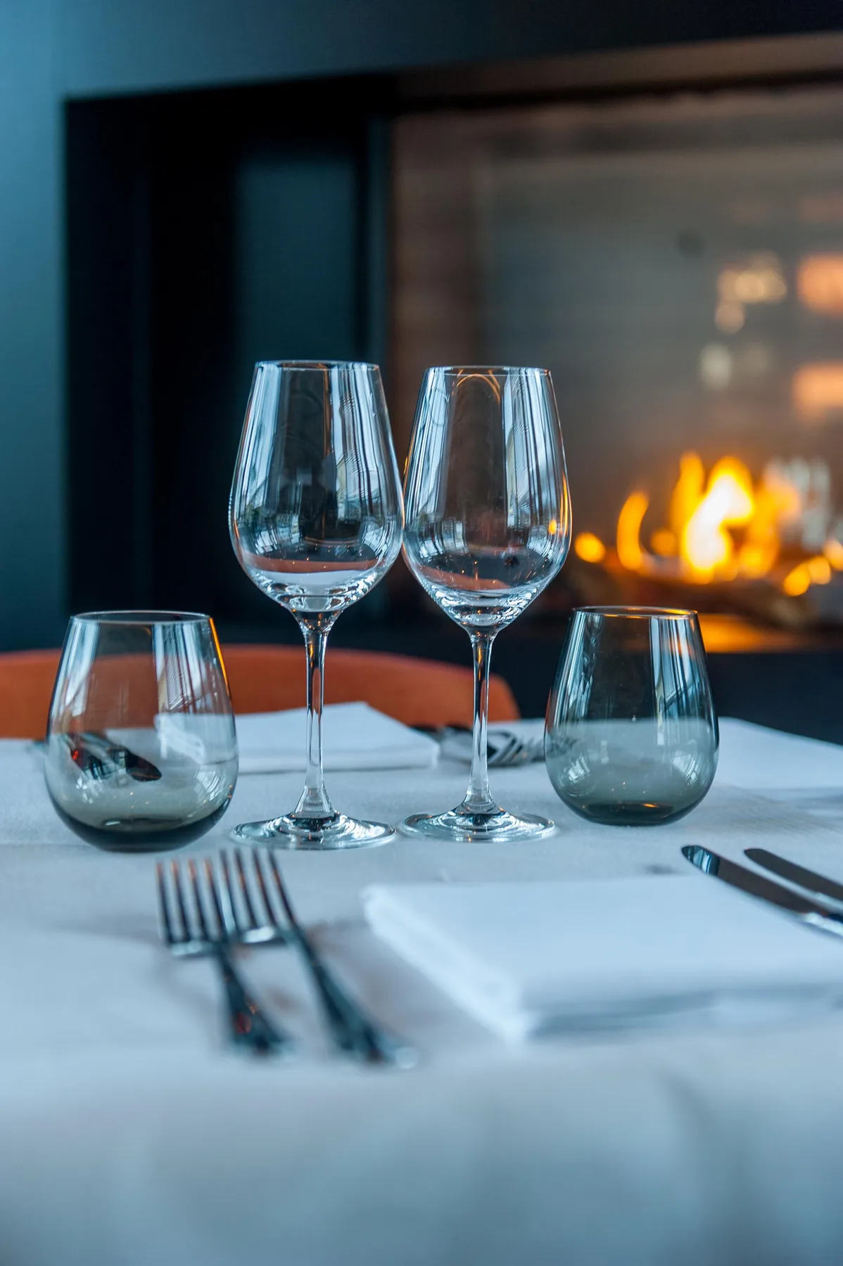 Espacio representativo del hotel: Una mesa de comedor está preparada con copas de vino frente a una chimenea encendida.