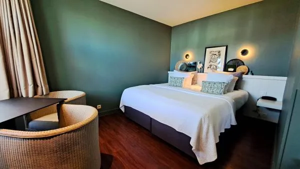Espacio representativo del hotel: Un dormitorio con una cama bien tendida y una silla tejida junto a la ventana.
