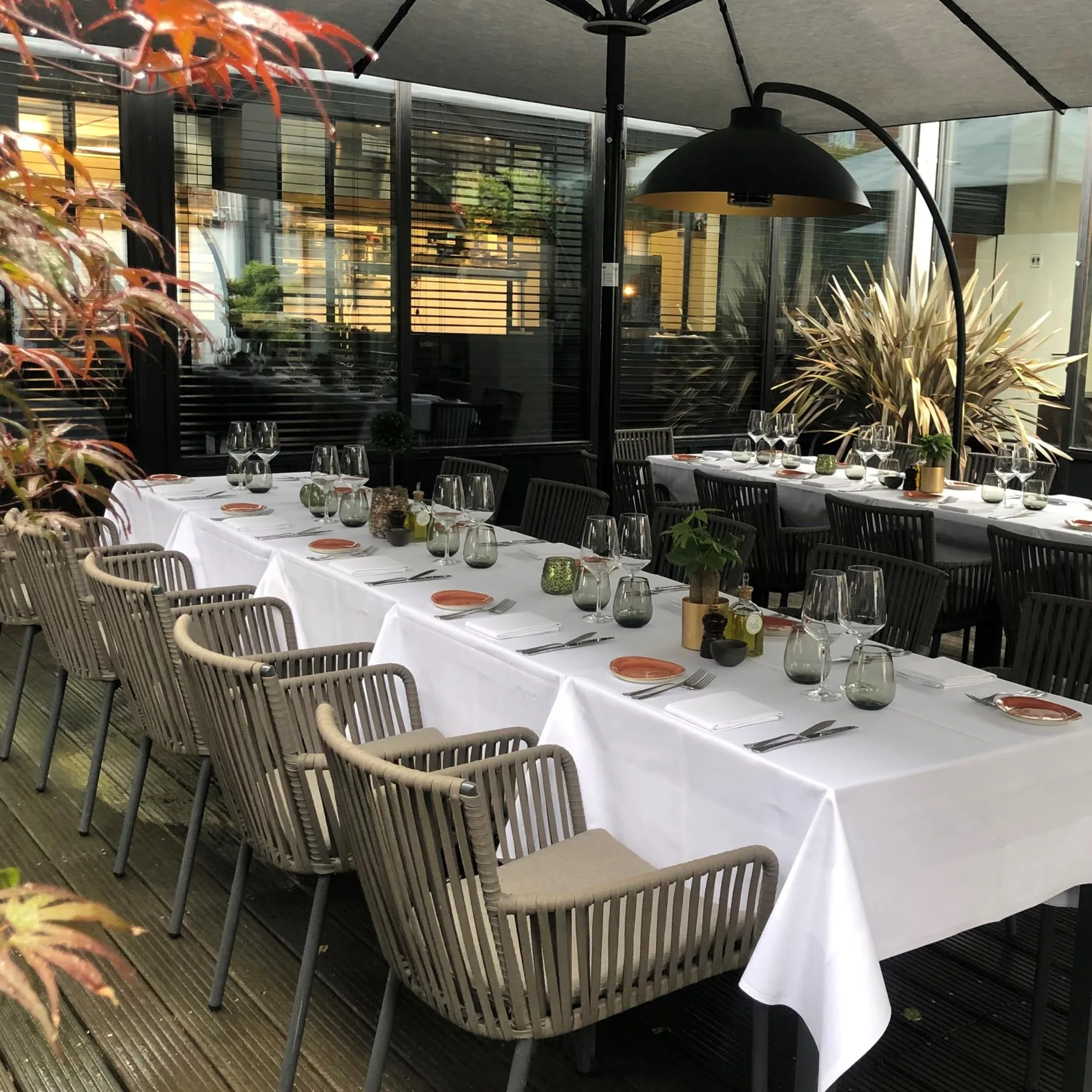 Espacio representativo del hotel: Una zona de comedor al aire libre tiene mesas largas con manteles blancos y cubiertos.