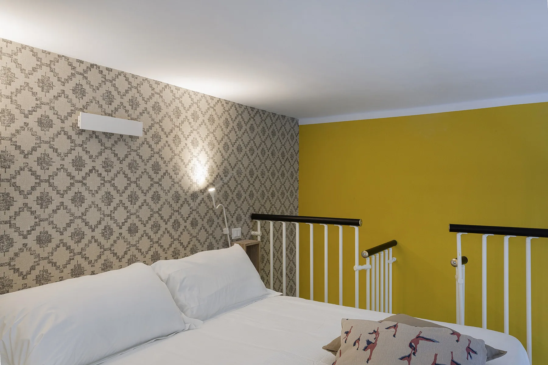 Un dormitorio con una cama junto a una pared con papel tapiz estampado y una pared amarilla.