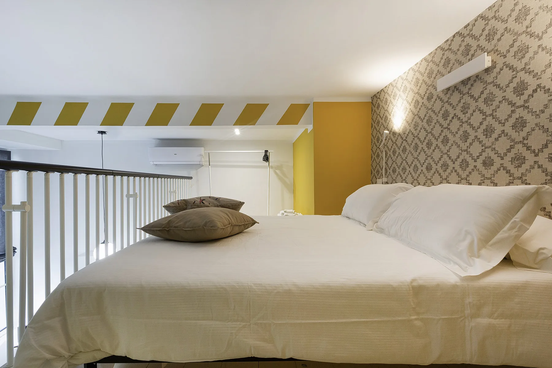 Un dormitorio con una cama, almohadas y papel tapiz estampado.