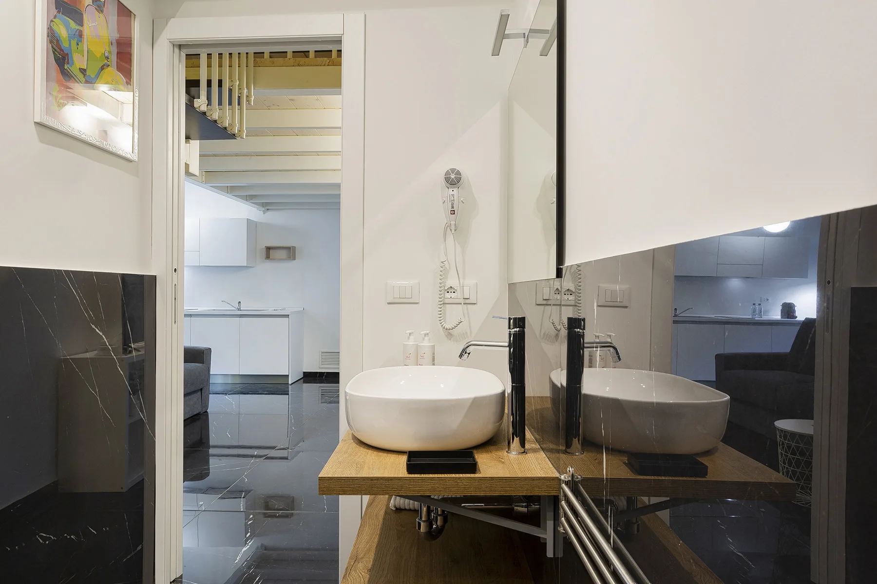Un mueble de baño con lavabo sobre encimera está frente a un espejo grande, junto a una puerta abierta.