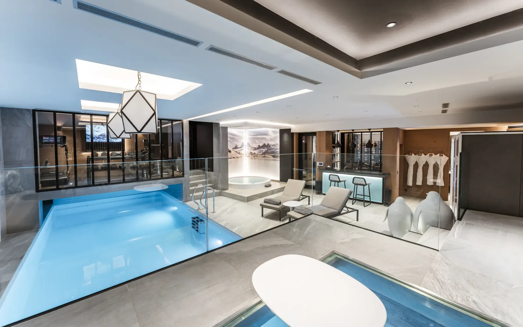 Una zona de piscina cubierta con paredes de cristal y un pequeño espacio para sentarse.