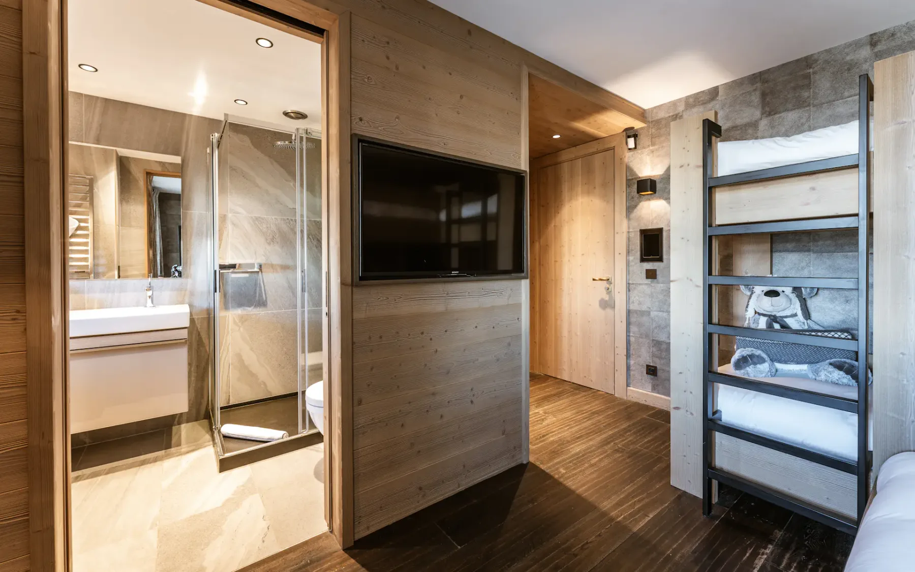 Un dormitorio moderno con televisión, literas y un baño contiguo.