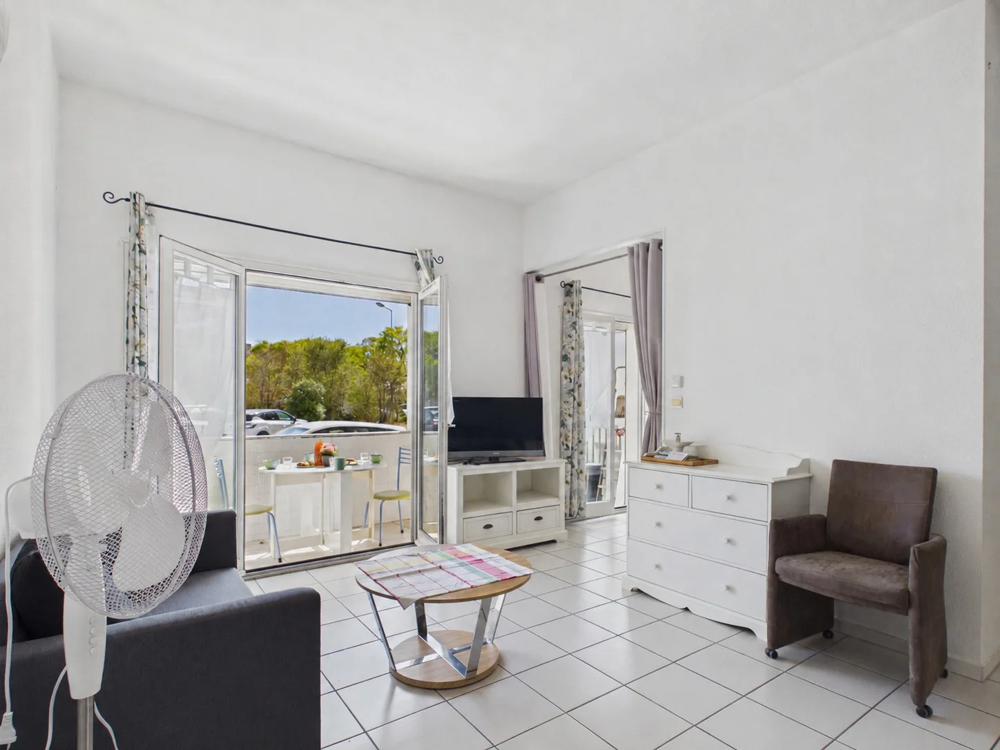 Bright living room with seating, a television, and an open balcony door.