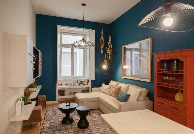Sala de estar con un sofá seccional crema, dos mesas de centro y paredes verde azulado oscuro.