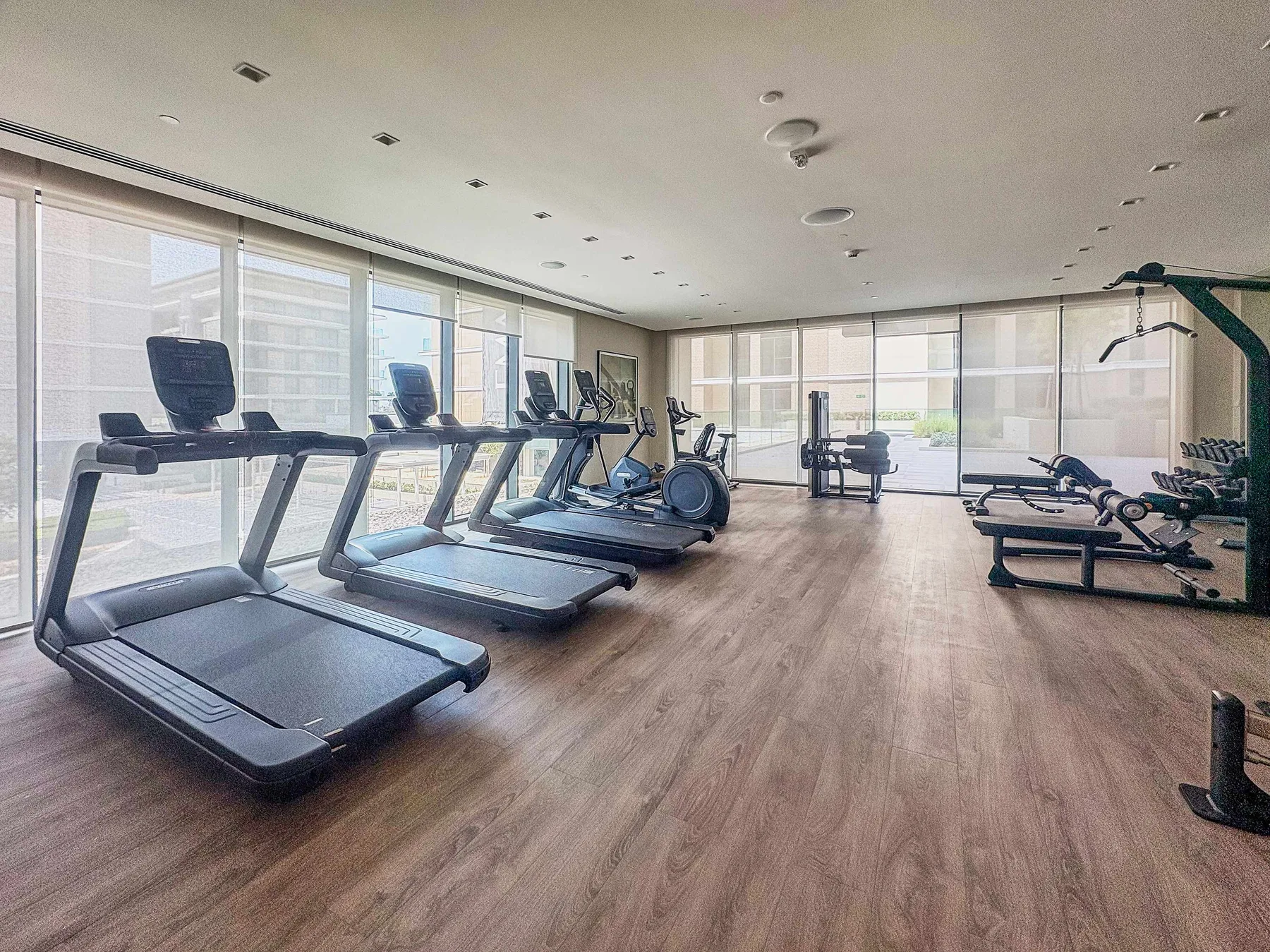 Zona común: Una sala de ejercicio luminosa con cintas de correr y equipos junto a grandes ventanales.