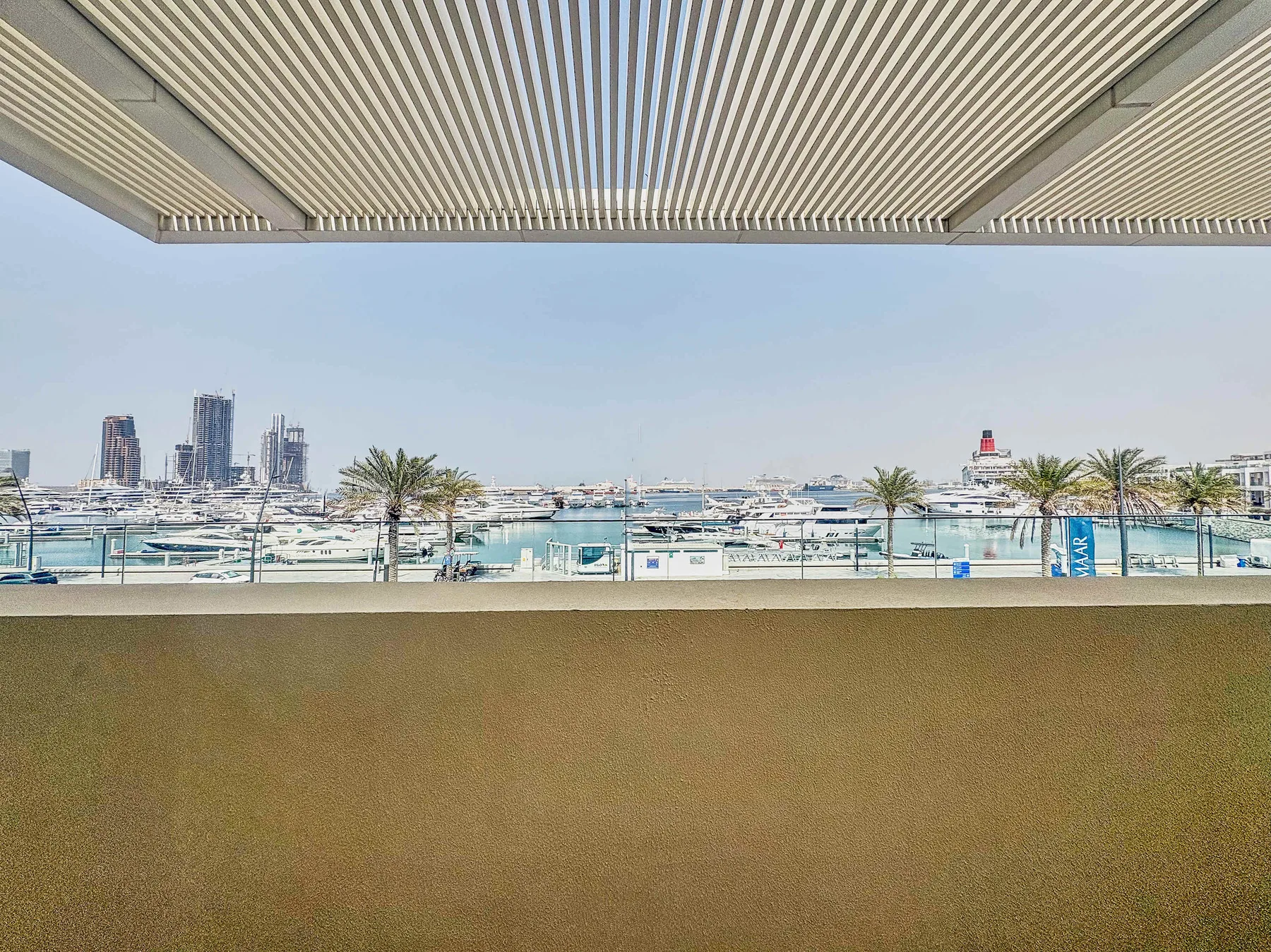 Zona común: Una terraza sombreada da a un puerto deportivo con barcos y edificios a lo lejos.