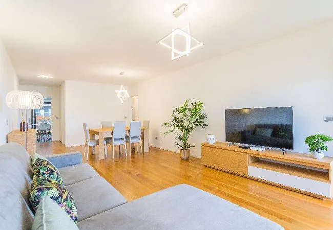Una sala luminosa con asientos, un televisor y un comedor.
