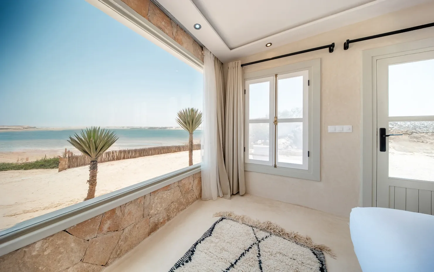 Representative hotel space: A bright room with a large window overlooking a sandy beach and the sea.