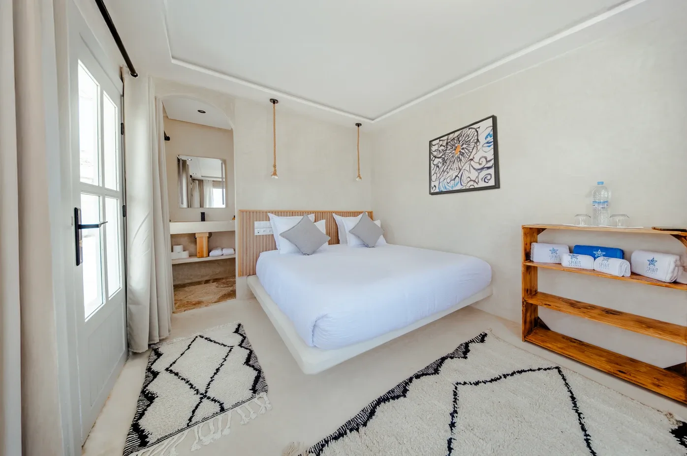 Representative hotel space: A bright bedroom with a bed, bedside shelves, and patterned rugs.