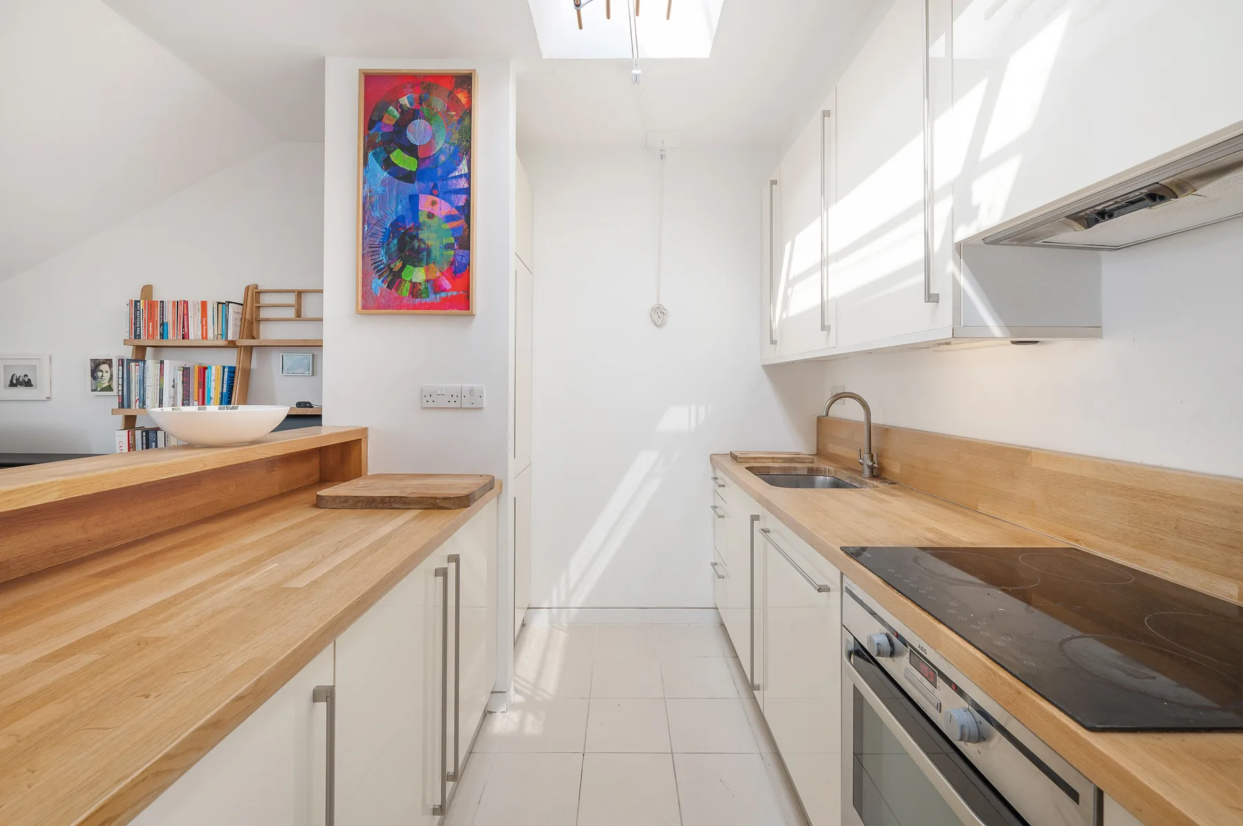 A bright kitchen with wooden countertops, white cabinets, and a central walkway.