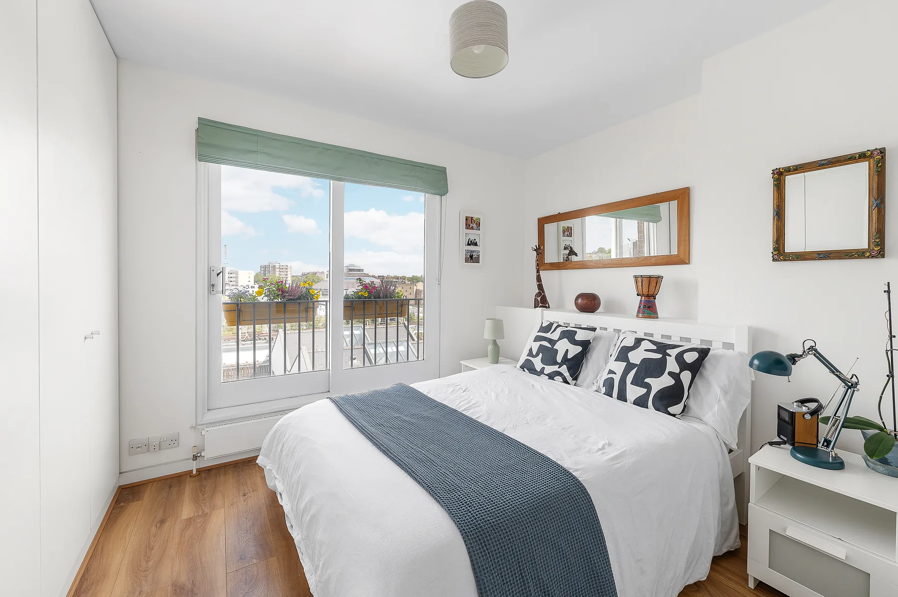 A bright bedroom with a neatly made bed beside a window overlooking a balcony.