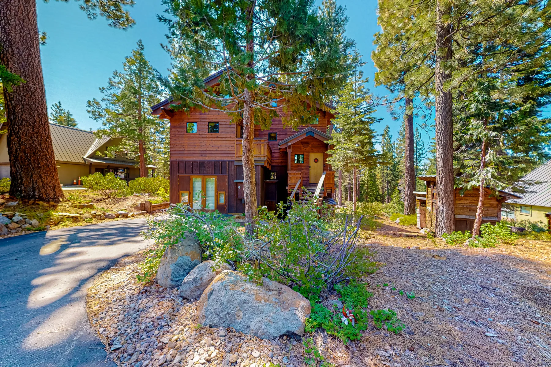 Una casa de madera está entre altos pinos, junto a un camino de grava.