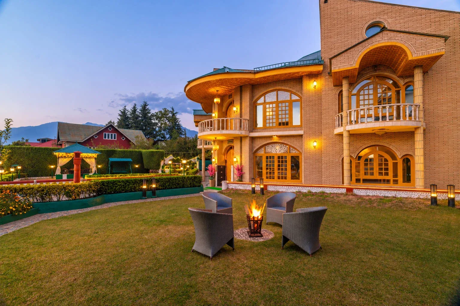 A brick building overlooks a grassy courtyard with outdoor seating and a small fire.