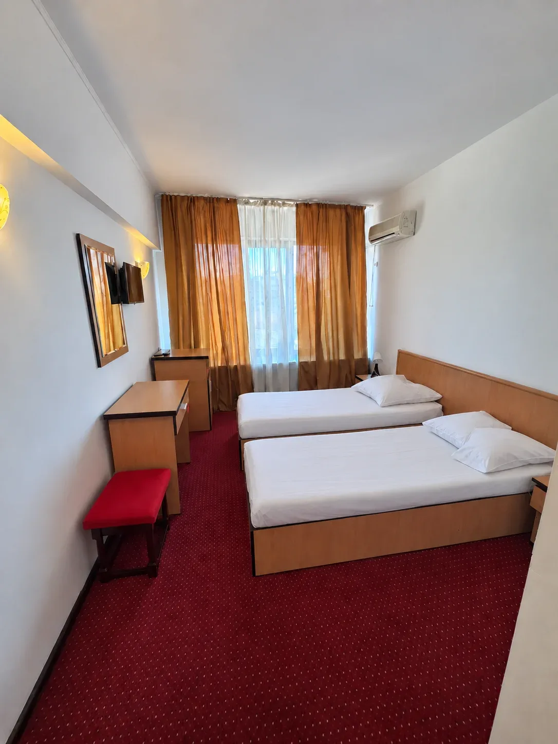 Espacio representativo del hotel: Un dormitorio de hotel con dos camas, un escritorio y cortinas naranjas.