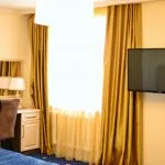 Espacio representativo del hotel: Un dormitorio con un televisor junto a una ventana cubierta por cortinas amarillas.