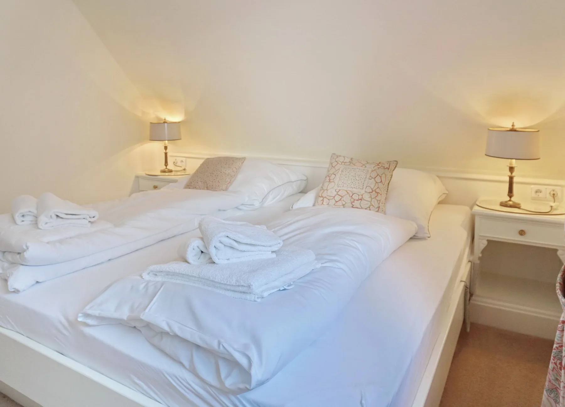 Un dormitorio luminoso con dos camas vestidas de blanco y lámparas de noche.