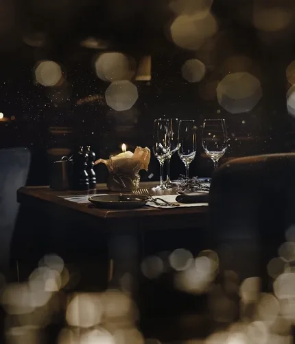 Espacio representativo del hotel: Una mesa de comedor con poca luz está preparada con platos, copas de vino y una vela.
