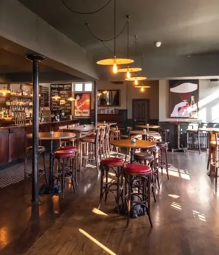 Espacio representativo del hotel: Zona de bar y comedor con mesas redondas, taburetes y lámparas colgantes.