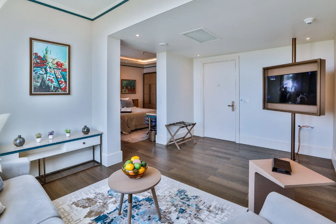 Espacio representativo del hotel: Sala de estar de una suite de hotel con asientos, una mesa de centro y un televisor en la pared.