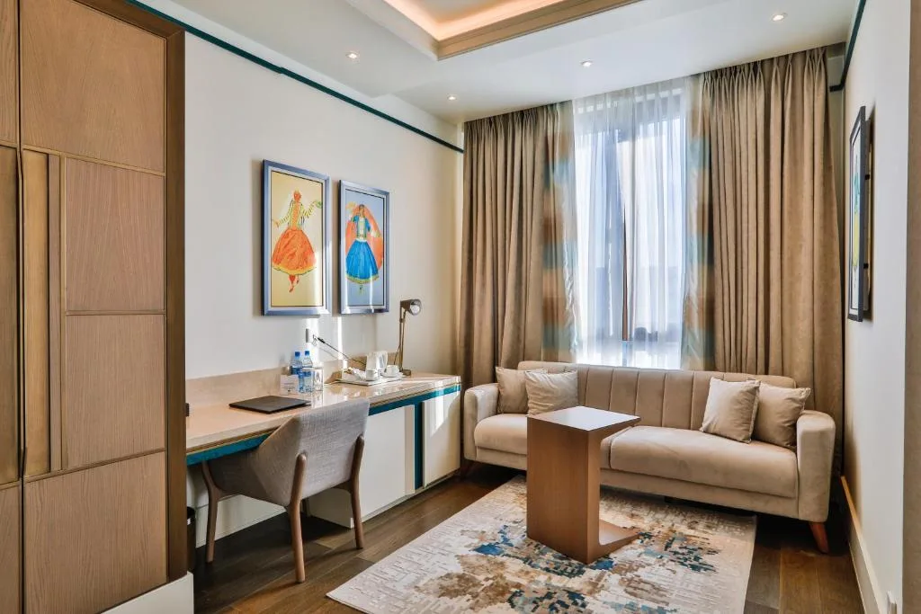 Espacio representativo del hotel: Una zona de estar con sofá, escritorio y mesa de centro junto a una ventana con cortinas.