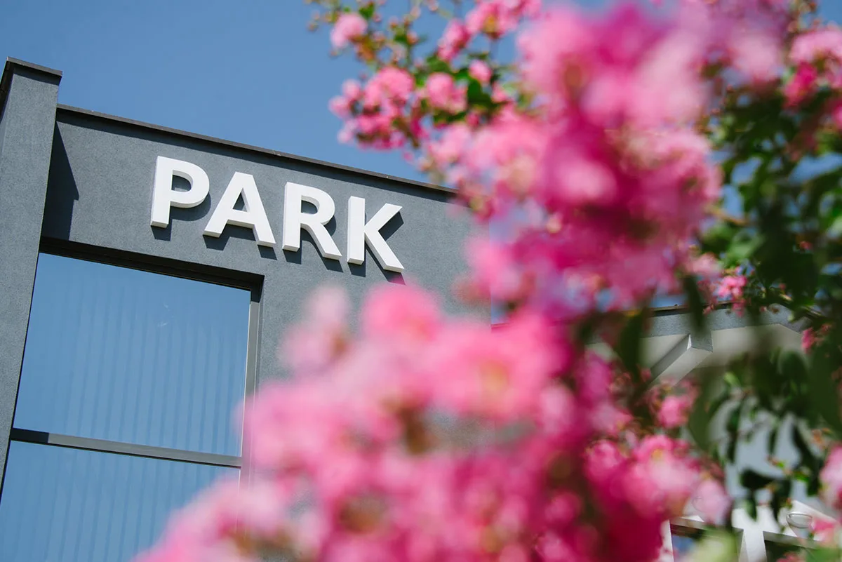 Espacio representativo del hotel: Rótulo exterior que dice «PARK», parcialmente enmarcado por flores rosadas.
