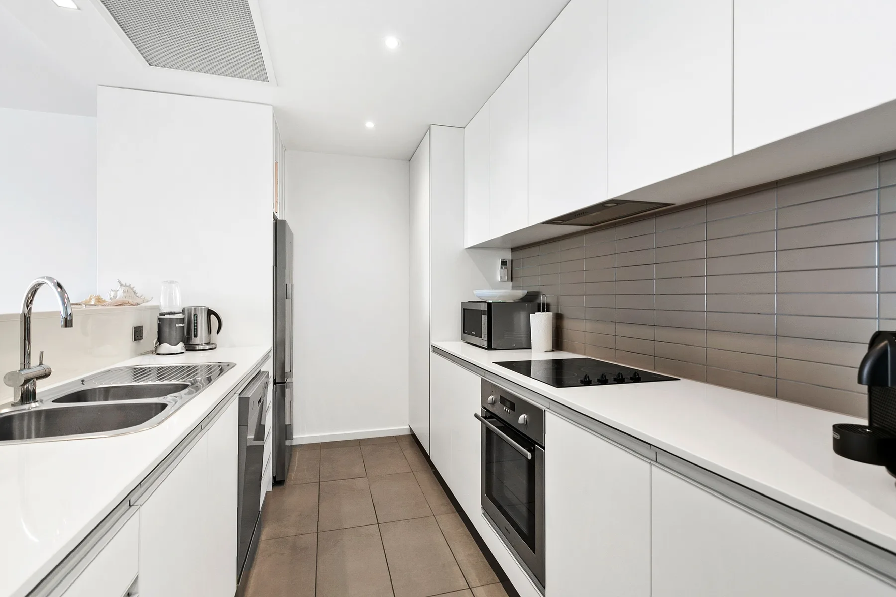 Una cocina moderna con gabinetes blancos, encimeras largas y electrodomésticos integrados.