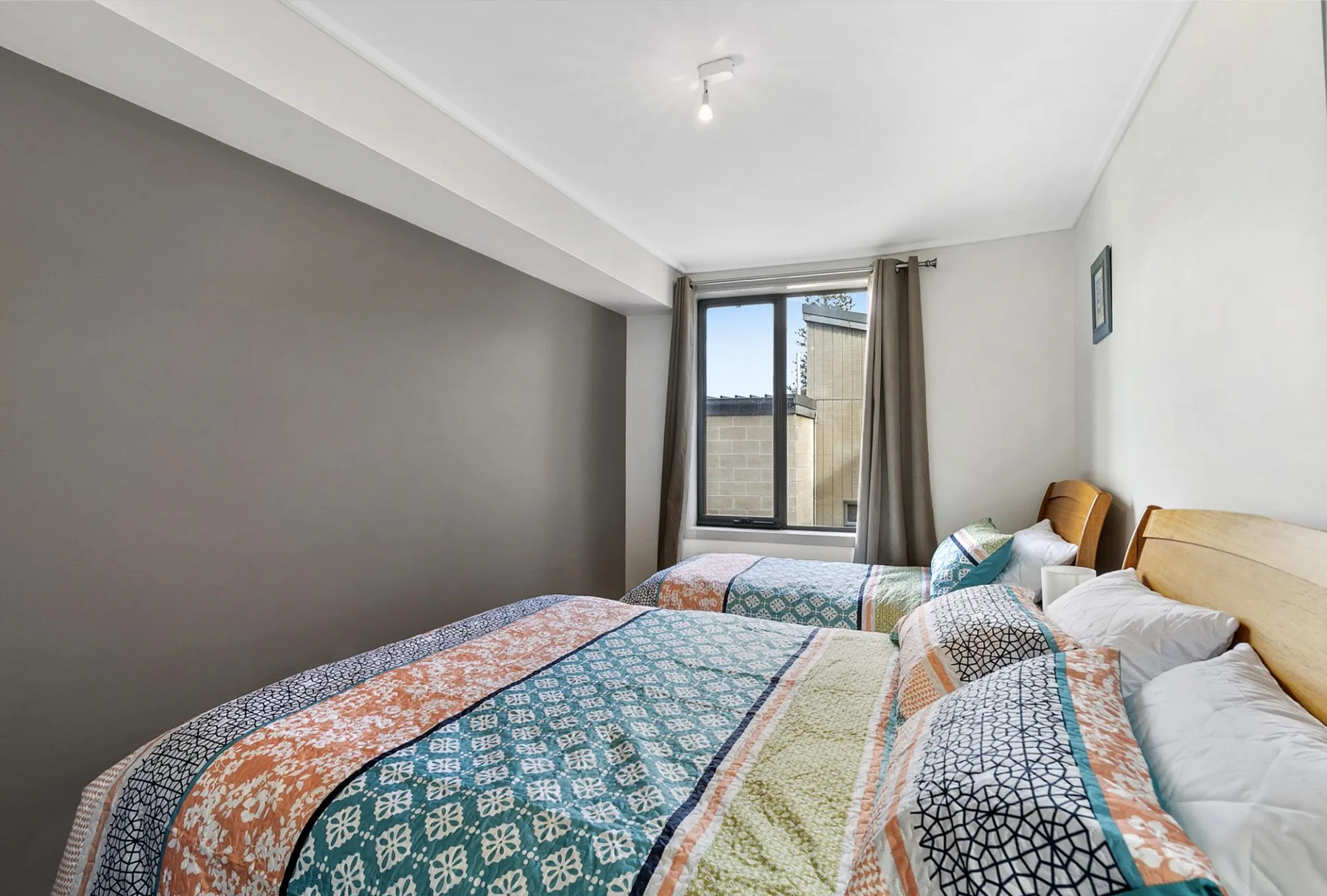 Un dormitorio con varias camas cubiertas de ropa de cama colorida y estampada junto a una ventana.
