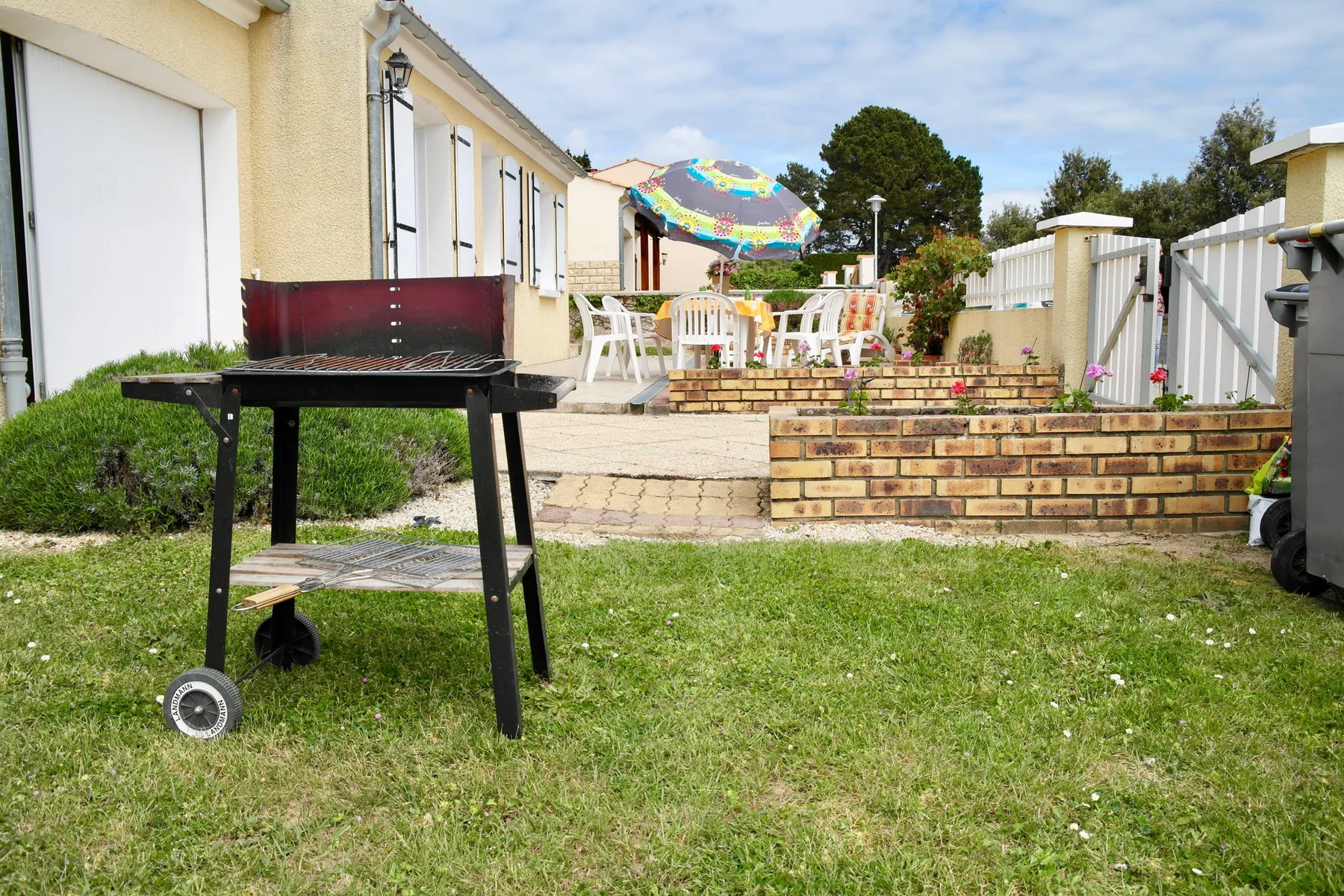 A garden patio with outdoor seating and a colorful umbrella beside a lawn.