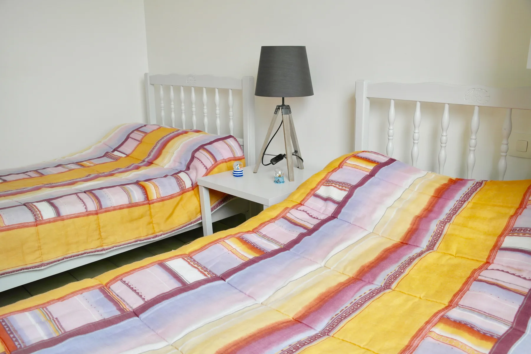 A bedroom with two beds covered in colorful striped bedding and a lamp between them.