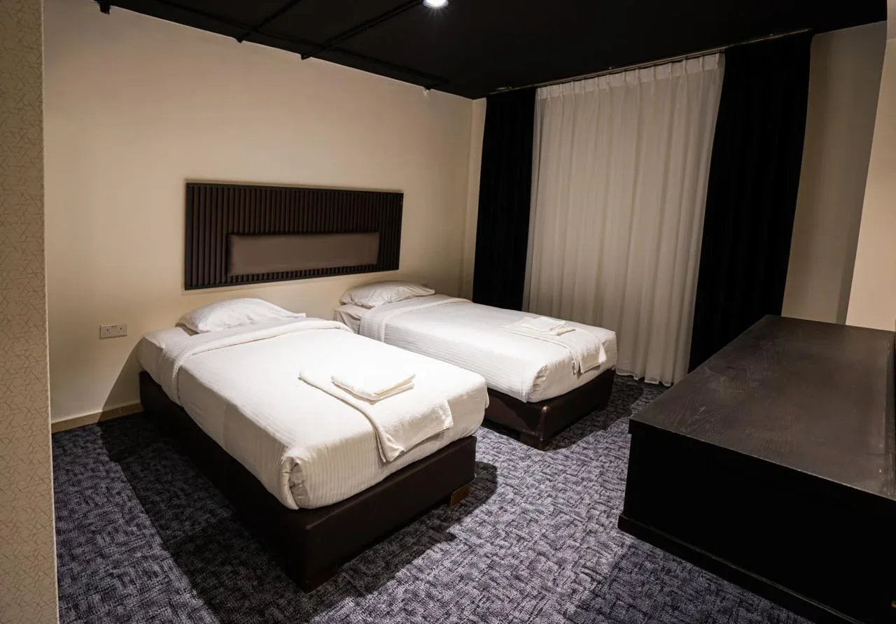 Espacio representativo del hotel: Un dormitorio de hotel con dos camas, alfombra estampada y una ventana con cortinas.
