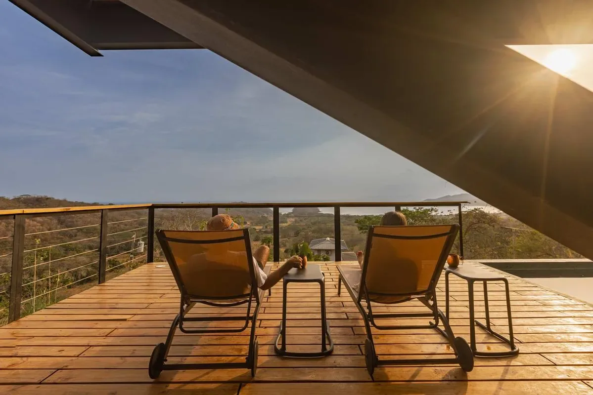 A wooden deck with reclining seating overlooks a green landscape in the evening sun.