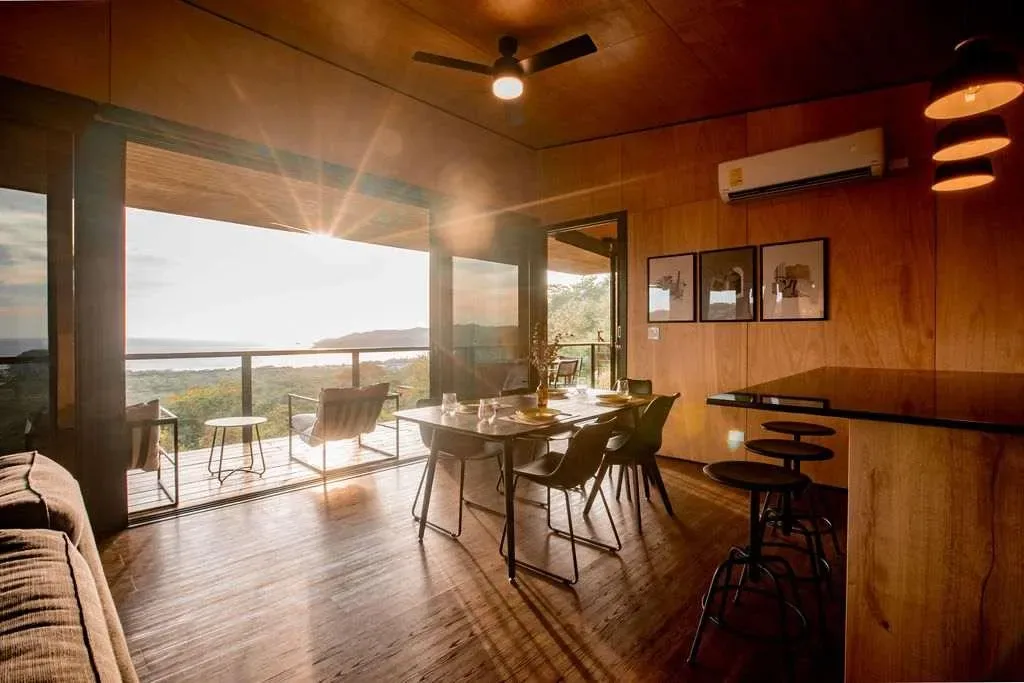 A dining area with a table and chairs beside large windows overlooking a landscape.