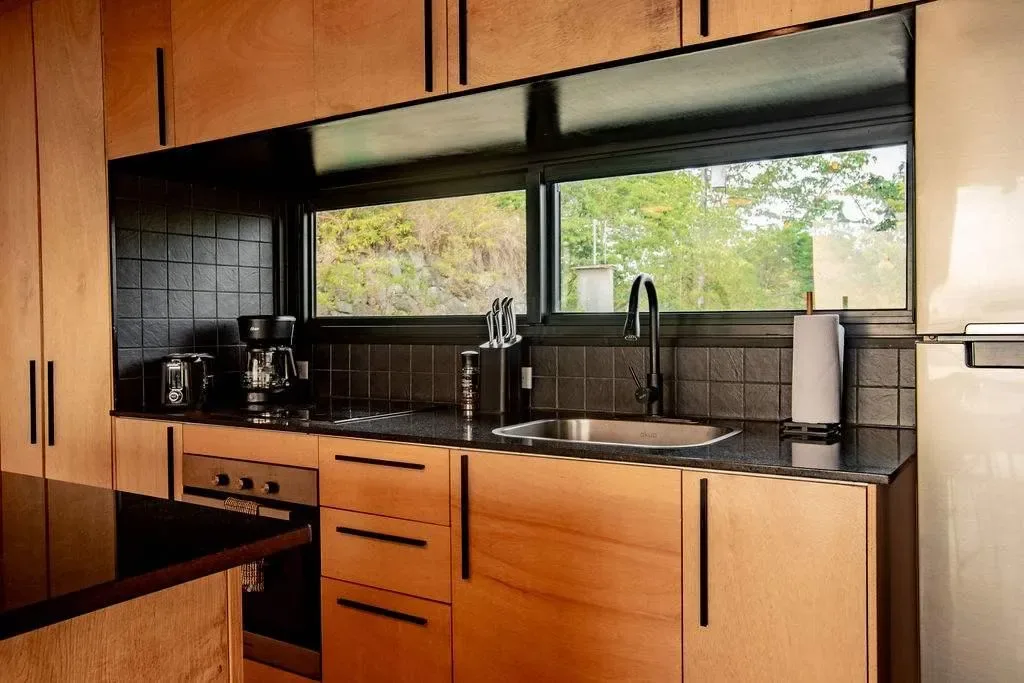 A kitchen with a sink and countertop beneath a wide window.