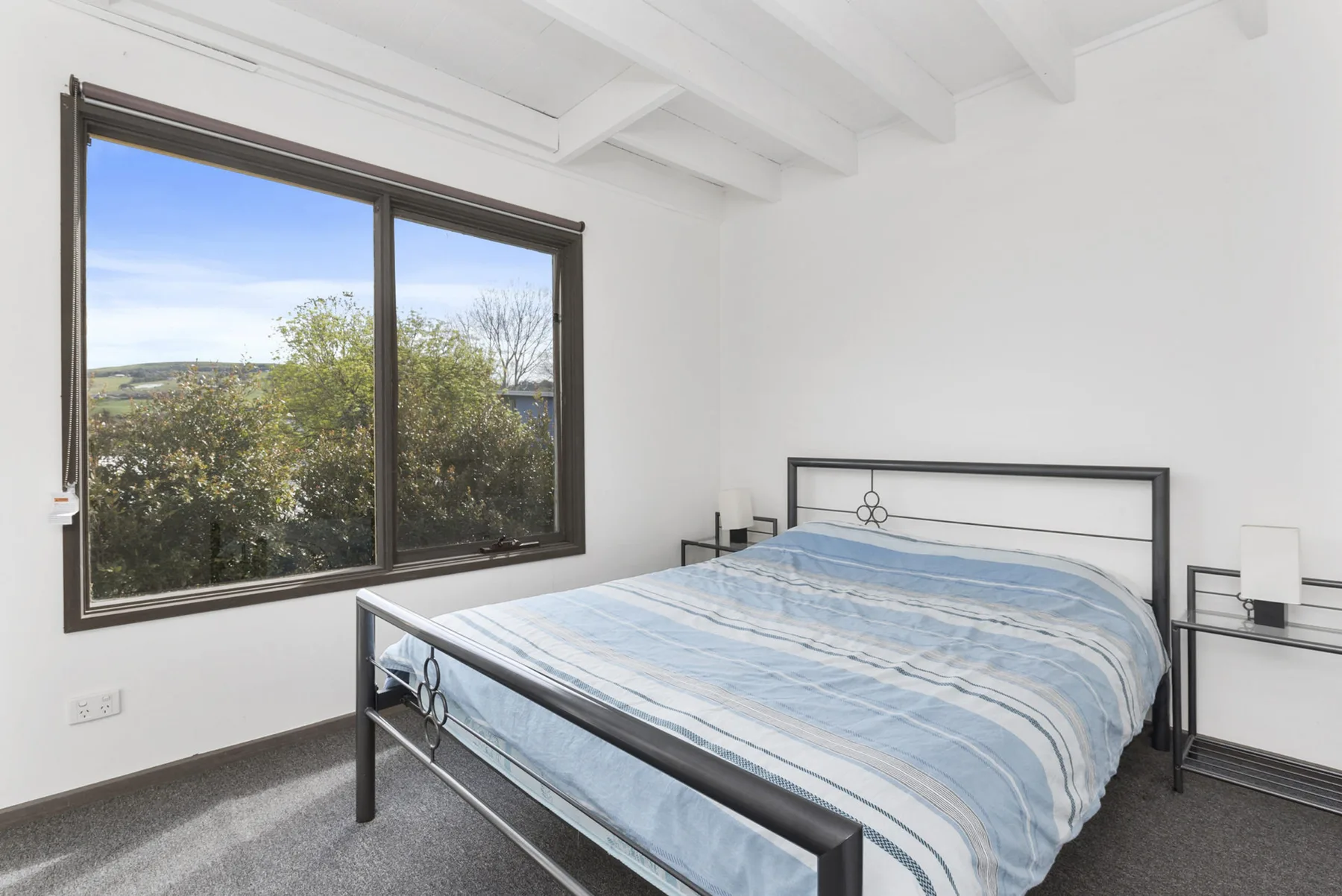 A bright bedroom with a bed beside a large window overlooking greenery.