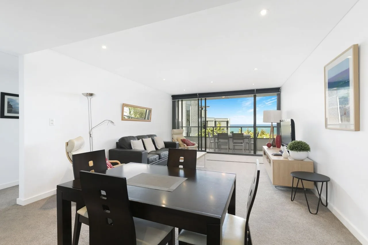 A bright living and dining area opens onto a balcony through wide glass doors.