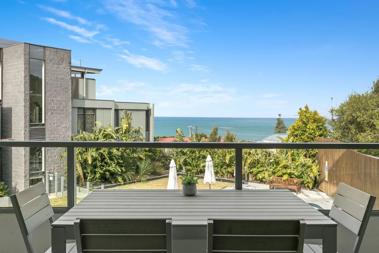 An outdoor deck with seating overlooks the ocean and surrounding greenery.