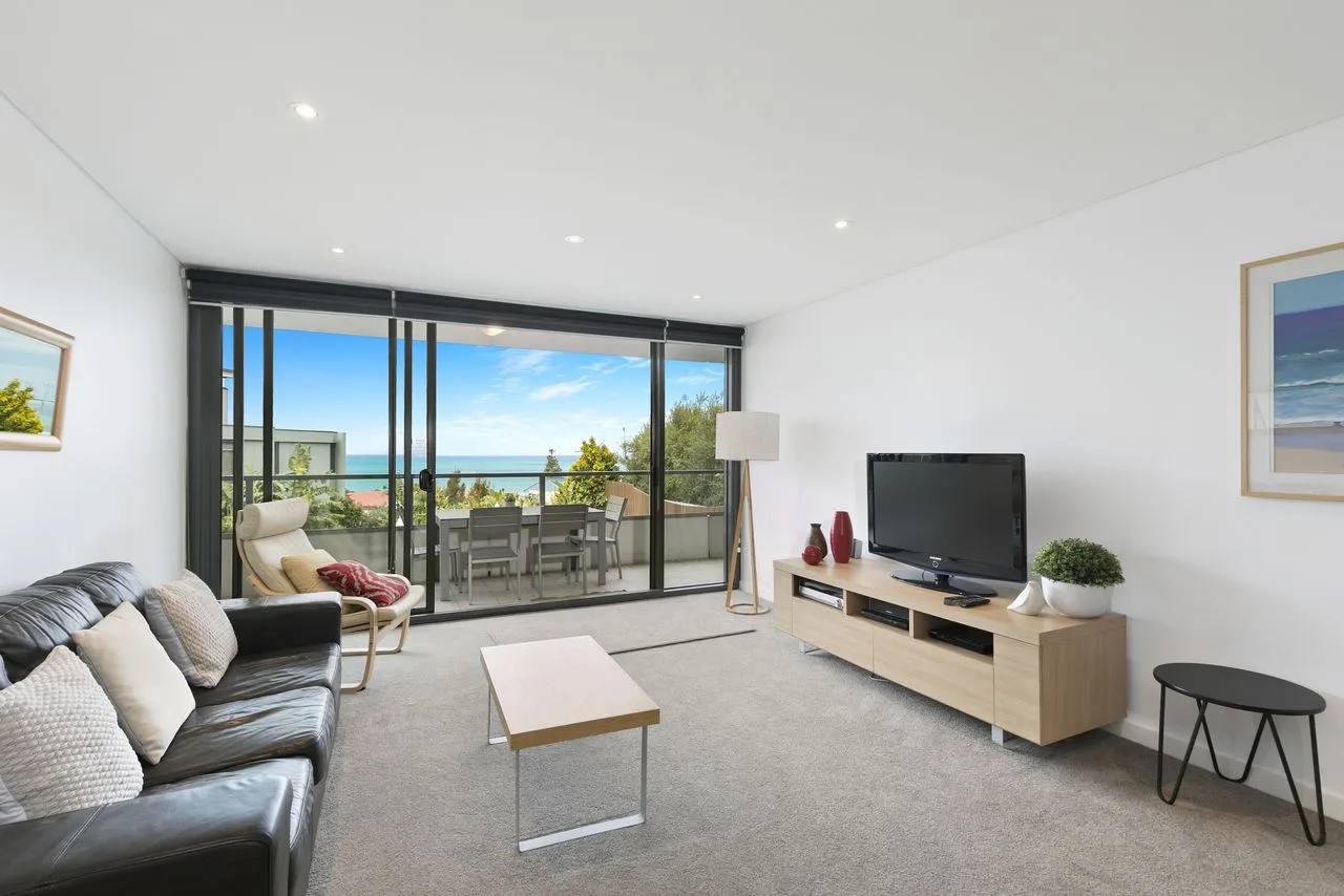 A bright living room with seating, a television, and sliding glass doors opening to a balcony.