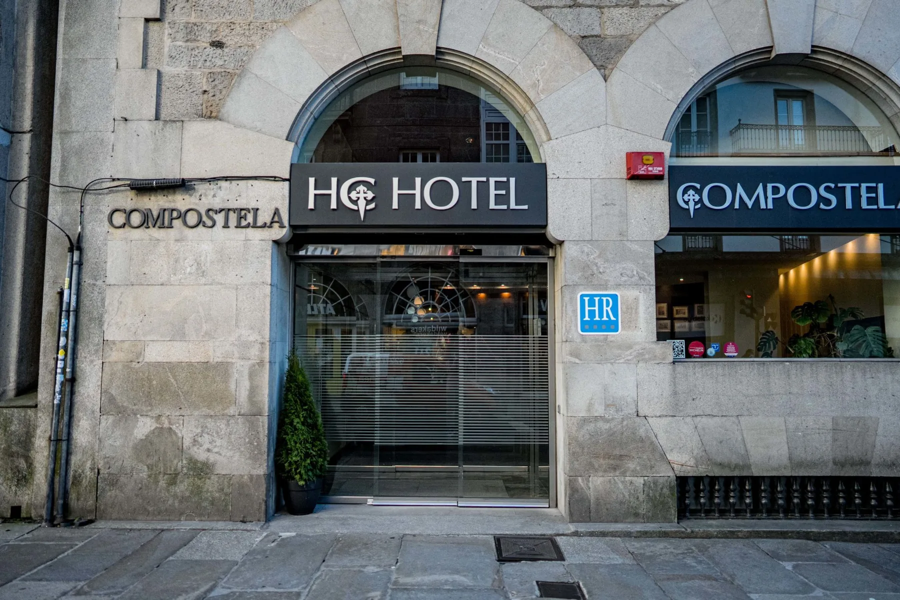 Espacio representativo del hotel: Fachada de piedra de un hotel con entradas arqueadas y escaparates de vidrio.