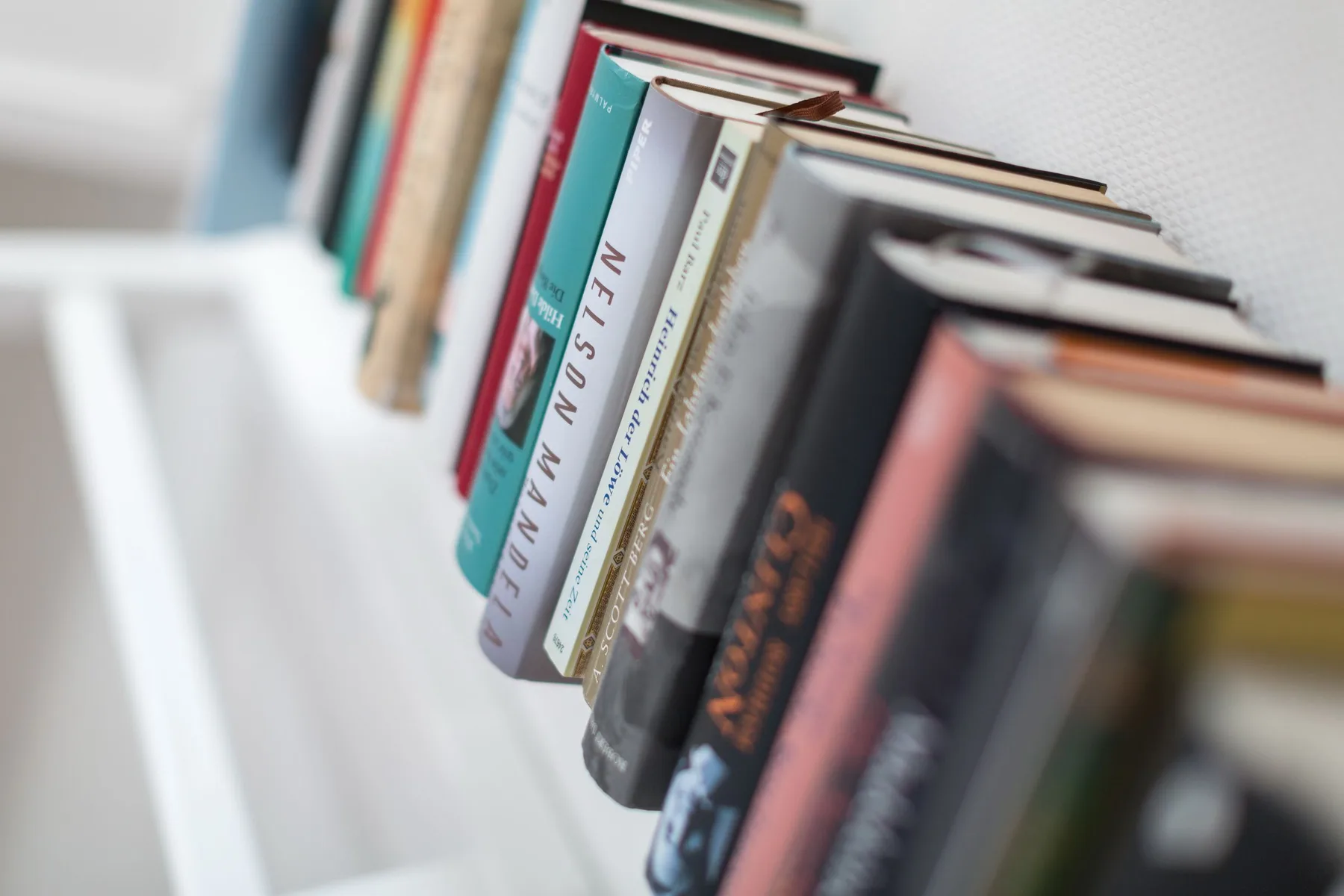 Libros alineados en un estante blanco, vistos de cerca.