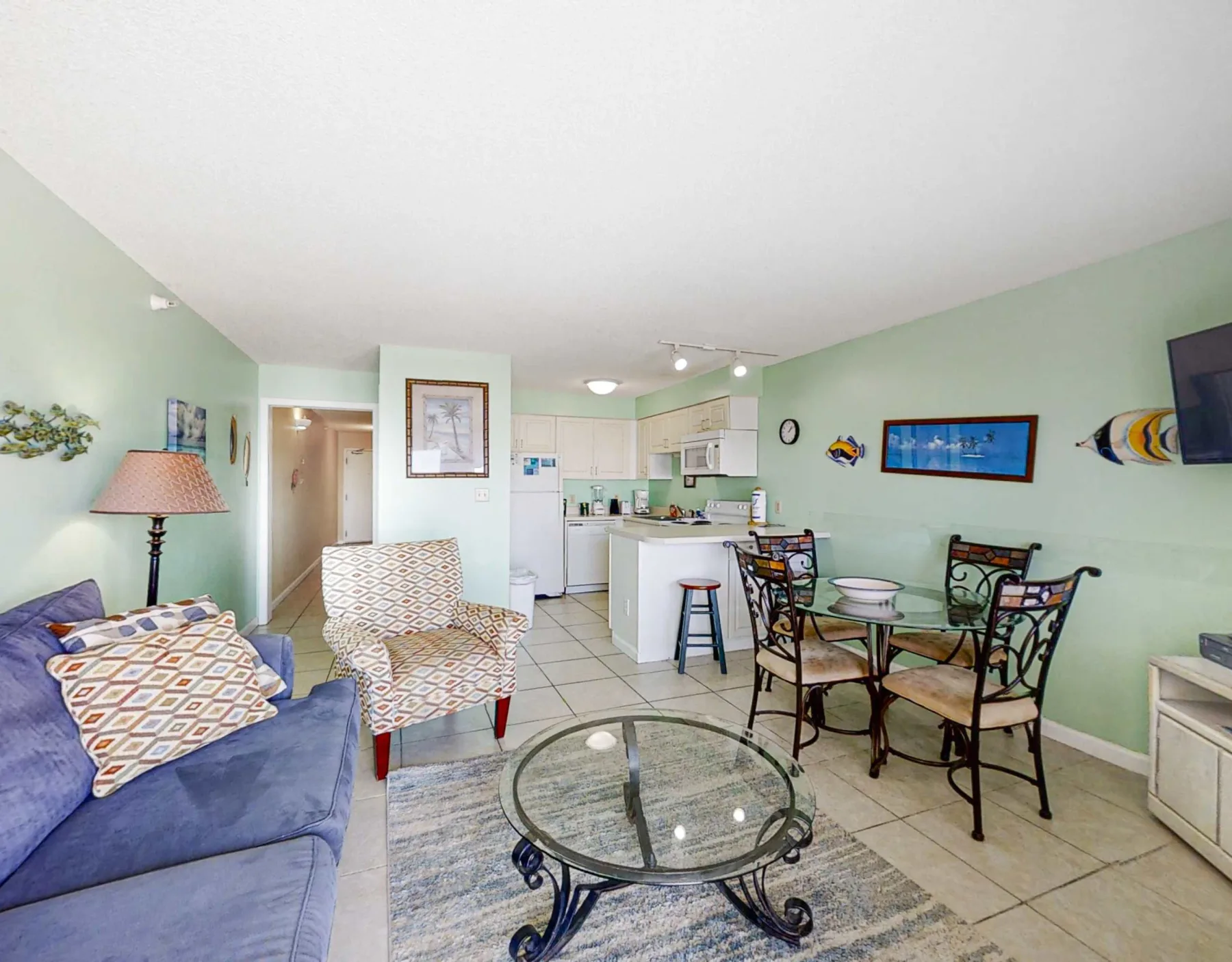 A living and dining area opens into a compact kitchen, with seating around a glass coffee table.