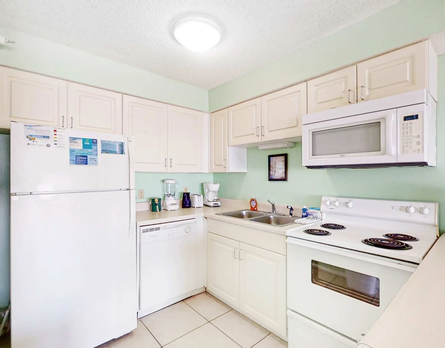 A bright kitchen with white cabinets and appliances around a tiled floor.